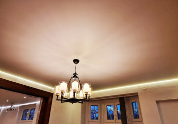 Ein stilvolles Zimmer mit einer Spanndecke, die von einer sanften indirekten Beleuchtung umrahmt wird. Die rustikale Einrichtung verleiht dem Raum eine zeitlose Eleganz.